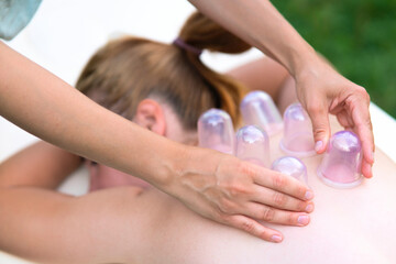 Woman masseur doing massage with vacuum cups on back outdoors. Cupping treatment at spa....