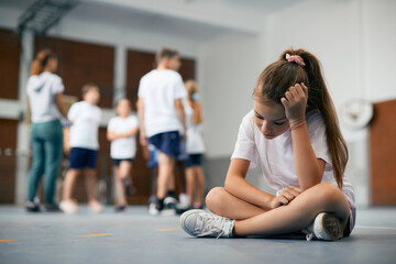 Fototapeta Sad schoolgirl feeling left out during physical activity class at school gym. obraz
