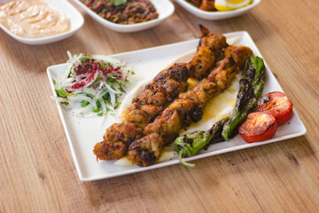 grilled chicken shish kebab with vegetables, mezzes and salads on wooden table. turkish barbecue. 