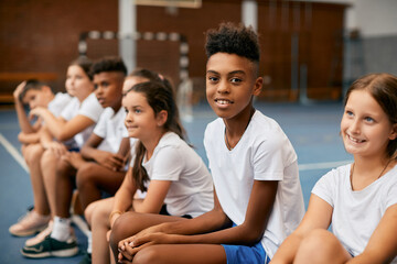 Happy African American boy and his schoolmates having PE class at school gym.