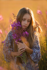 A child in a hat with a bouquet flowers. A girl in dress, a straw hat, with a bouquet is standing on a flower meadow. Summer time.