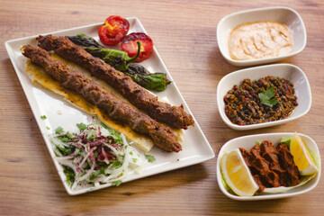 grilled meat lamb shish kebab with vegetables, mezzes and salads on wooden table. adana, urfa kebap. turkish barbecue.
