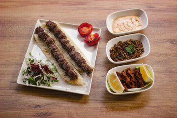 grilled meat lamb shish kebab with vegetables, mezzes and salads on wooden table. adana, urfa kebap. turkish barbecue.