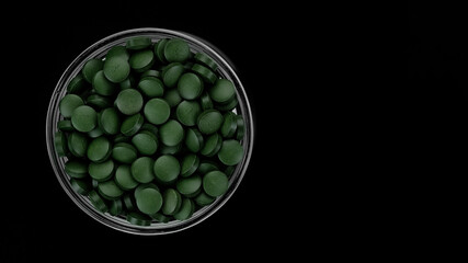 Green pills on black background. superfoods Spirulina, chlorella supplement green pills top view