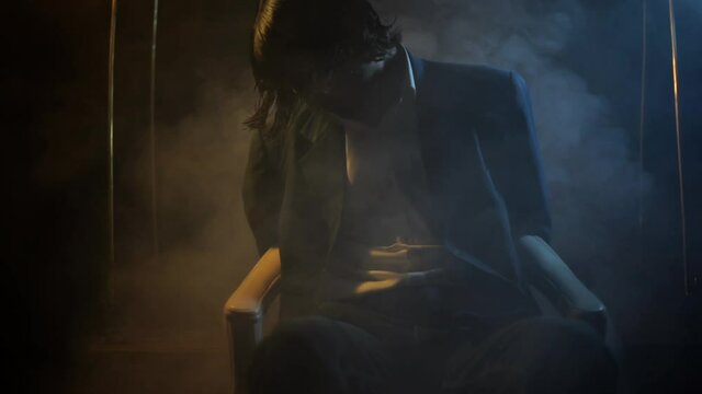 Steady shot of a businessman tied on chair sitting with dramatic lighting and some smoke coming from the bottom of the frame in high resolution.
