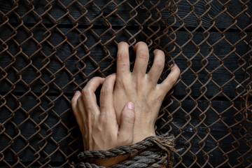 female hands tied with stars rope hold on to a metal fence, imprisonment, slavery