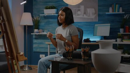 Black young artist working on vase drawing at home in artwork studio. African american woman using art tools, pencil and white canvas on easel creating authentic masterpiece as hobby