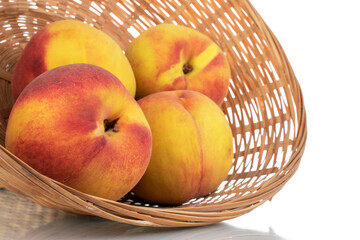 Several ripe peaches in a straw bowl, close-up, isolated on white.