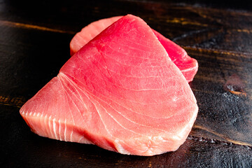 Raw Tuna Steaks on a Dark Wood Background: Closeup view of uncooked tuna steaks on a wooden table