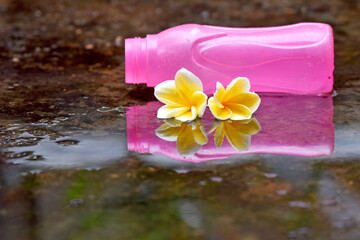 Frangipani flower and pink bottle as a background with clear water reflection
