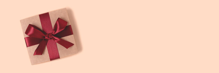 Gift box tied with red ribbon on a beige background. Holidays concept with copyspace.