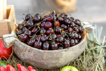 Ripe cherries are lying in a wooden cup on the table.