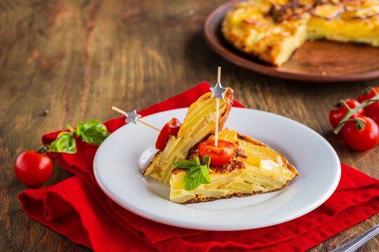 Sliced Spanish tortilla, a traditional dish with eggs and fried potatoes on a clay plate on a wooden background. Potato recipes.