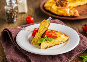 Sliced Spanish tortilla, a traditional dish with eggs and fried potatoes on a clay plate on a wooden background. Potato recipes.
