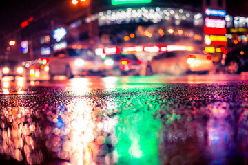 Rainy night in the big city, dense traffic at a busy intersection in the light of shop windows. View from the level of asphalt