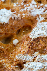 Macro shot on traditional round artisan bread loaf in a cast iron skillet with sprinkled flour and banneton spiral texture. Fresh loaf of homemade bread with golden color, hot from the oven on a towel