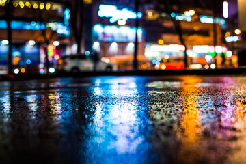 Rainy night in the big city, city alley with trees near the loaded avenue with shops. View from the...