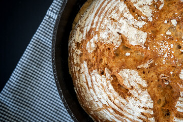 Closeup on traditional round artisan bread loaf in a cast iron skillet with sprinkled flour and...