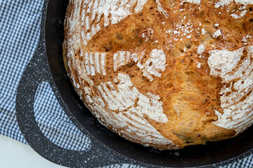 Closeup on traditional round artisan bread loaf in a cast iron skillet with sprinkled flour and...