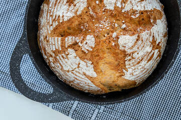 Traditional round artisan bread loaf in a cast iron skillet with sprinkled flour on top and...