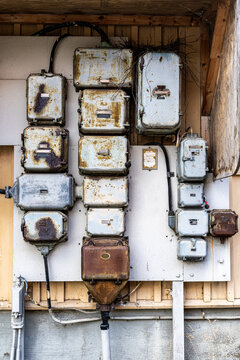 Outdoor closeup facade view of many old rusty worn electrical boxes and wires on building wall.