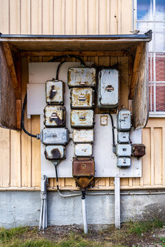 Outdoor closeup facade view of many old rusty worn electrical boxes and wires on building wall.