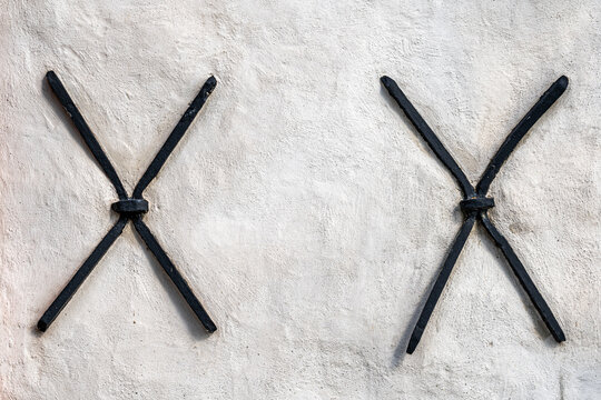 Two old black anchient iron steel cross anchors on a white stone building exterior wall.