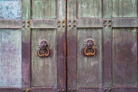 Closeup of two massive bronze and copper doors with green tint, knockers in shape of lions.