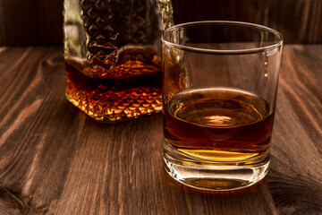 Decanter of whiskey and a glass on a wooden table. Angle view