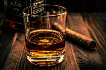 Bottle of whiskey and a glass with cuban cigar on a wooden table