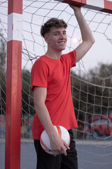 Jugador de futbol jóven con una sonrisa posando sentado en la pista con el balon en la red de la...