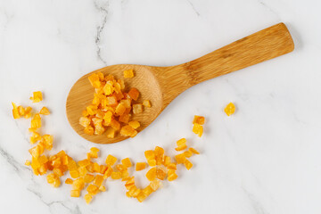 Candied orange peels on wooden spoon and  white marble table. Light background with copy space