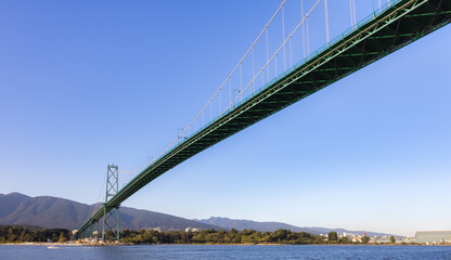 View of the Famous Lions Gate Bridge from Stanley Park in a modern city. Downtown Vancouver, British Columbia, Canada. Sunny Summer Sunset.