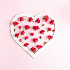 A white heart-shaped frame filled with tiny red roses and buds. Minimal love concept on bright pink backgrounds