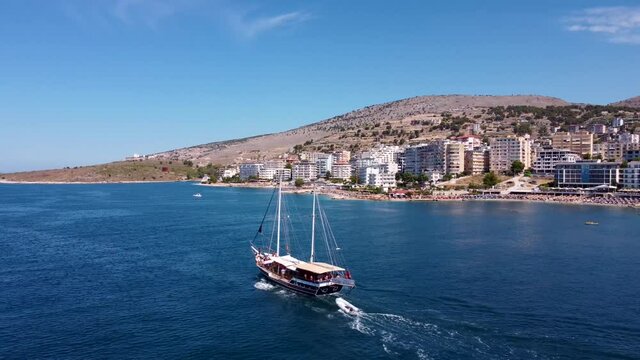 An old two-masted ship sails on the waves of the Ionian Sea against the backdrop of the city