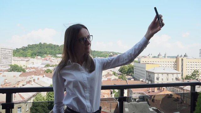 An attractive brunette woman makes a selfie outdoors on terrace with old city view. Lifestyle concept