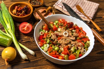 Tasty tuna salad with vegetables on wooden table. Vegetable salad with tuna. Preparing a healthy vegetable salad with fish. Diet food for athletes.