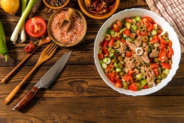 Tasty tuna salad with vegetables on wooden table. Vegetable salad with tuna. Preparing a healthy vegetable salad with fish. Diet food for athletes.