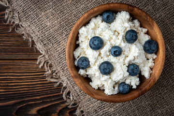 Cottage cheese and blueberry in wooden bowl and spoon on dark wooden background.