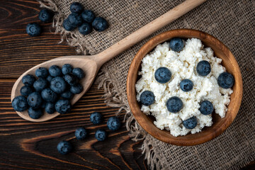 Cottage cheese and blueberry in wooden bowl and spoon on dark wooden background.