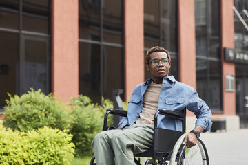 Pensive young Black man in eyeglasses spinning wheel of wheelchair while walking alone