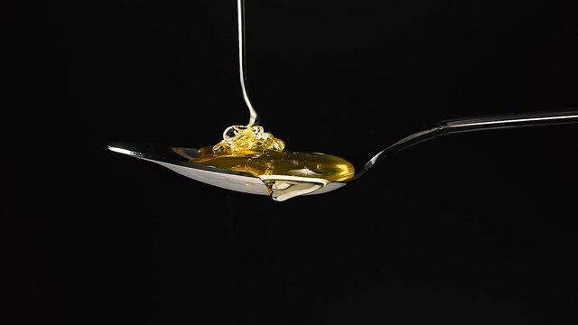 Close up honey flowing from metal spoon on black