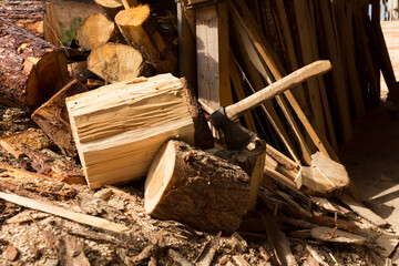An axe, surrounded by many kinds of logs, resting on a chopping block. 