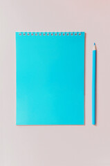 open notebook for notes with a blue pencil on a pink background top view