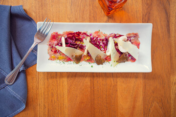 Tuna carpaccio with purple cabbage and sliced parmesan cheese. Carpaccio wooden table in restaurant. Sunny lunchtime