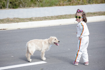Linda criança com roupa branca e óculos de sol brincando com cachorro Golden Retriever .
