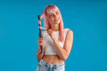 Happy woman smiling at camera while styling pink long straight hair using curling iron, standing...