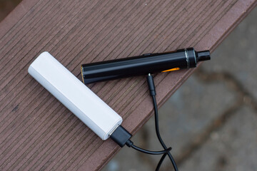 Power bank and charges an electronic cigarette on a wooden bench.