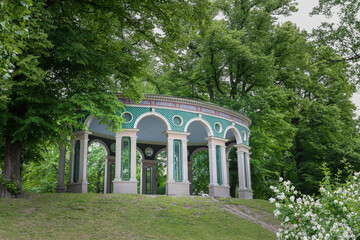 Pavilion standing on a hill in a public park in Stockholm, Sweden. Large oak trees surround the structure.