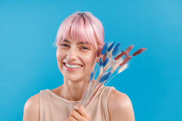 Happy woman with pink hair smiling at camera, holding dried pampas grass in her hand. Reed stem,...